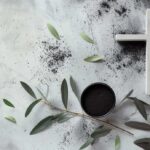 Cruz postrada sobre marmol junto a tierra y plantas de un olivo