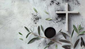 Cruz postrada sobre marmol junto a tierra y plantas de un olivo